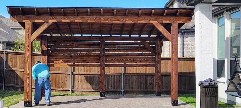 Crew member fastening a freestanding cedar pergola next to a backyard pool