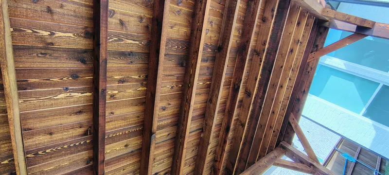 Stained cedar rafters of a freestanding pergola, seen from below